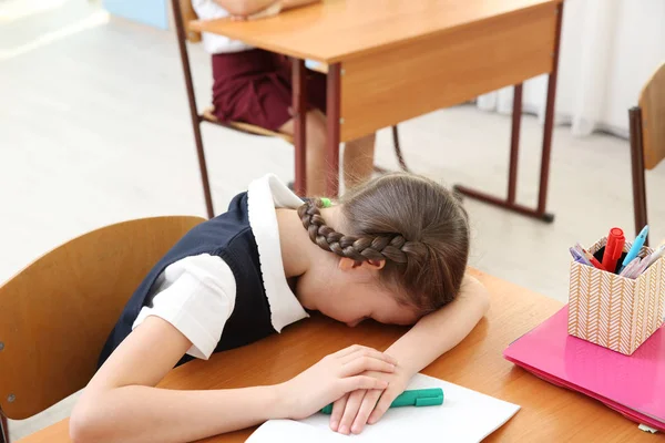 Portrait of tired elementary schoolgirl sleeping on desk in classroom — Stock Photo, Image