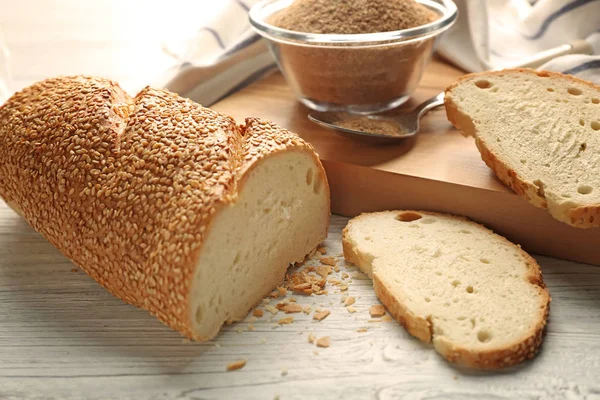 Sliced loaf and glass bowl of bread crumbs on wooden table — Stock Photo, Image