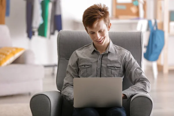 Evde kol-sandalyede otururken dizüstü bilgisayar ile çalışan genç — Stok fotoğraf