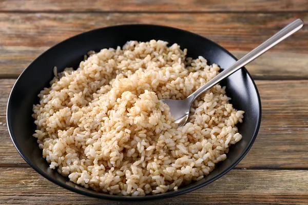 Assiette avec riz brun sur fond de table en bois — Photo