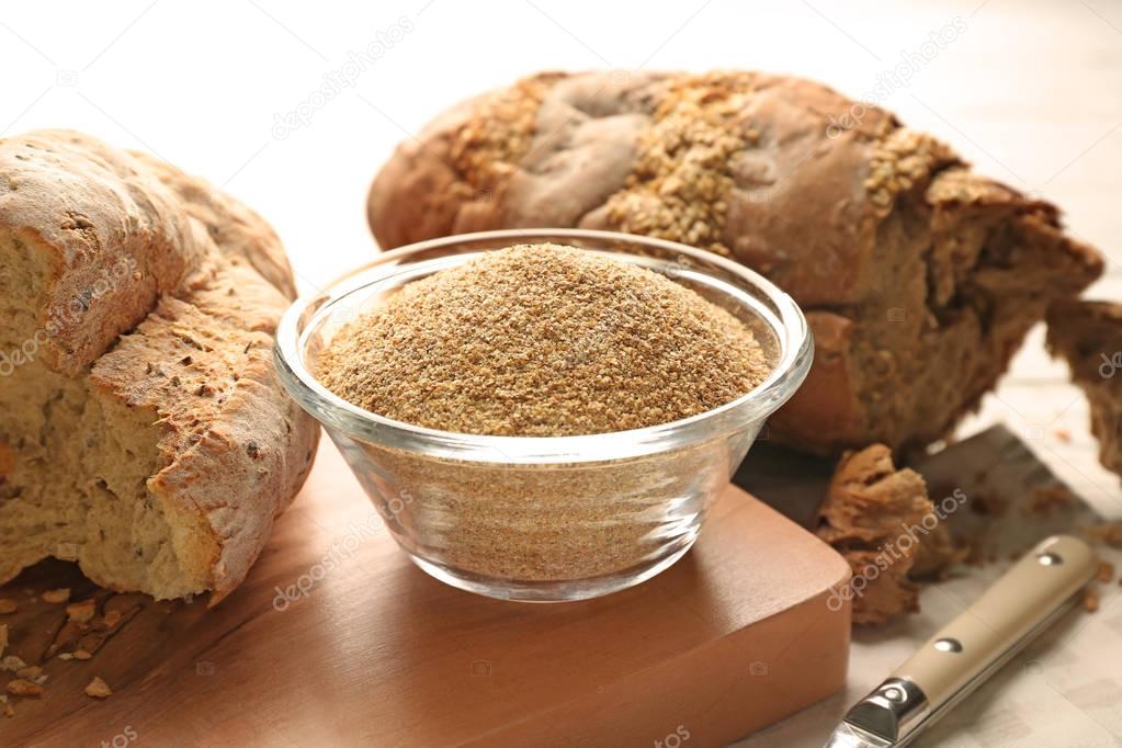 Glass bowl of bread crumbs and broken loafs on wooden board