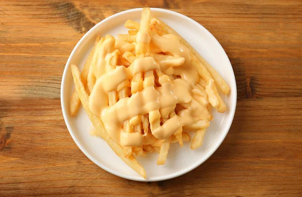 Placa con sabrosas papas fritas de queso sobre fondo de madera — Foto de Stock
