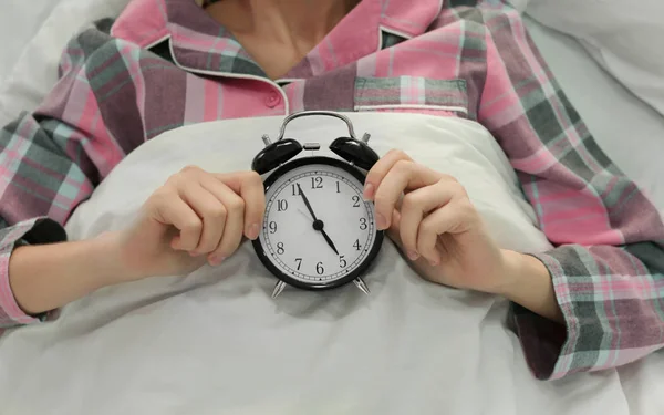 Mujer joven con despertador acostada en la cama en casa. Concepto de trastorno del sueño —  Fotos de Stock