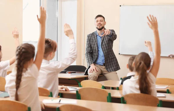 Alumnos escuchando al maestro y levantando las manos para responder en el aula —  Fotos de Stock