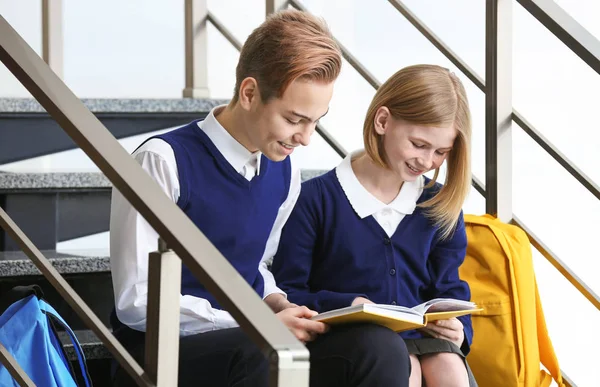 Симпатичные мальчик и девочка в школьной форме сидят на лестнице и читают книгу — стоковое фото