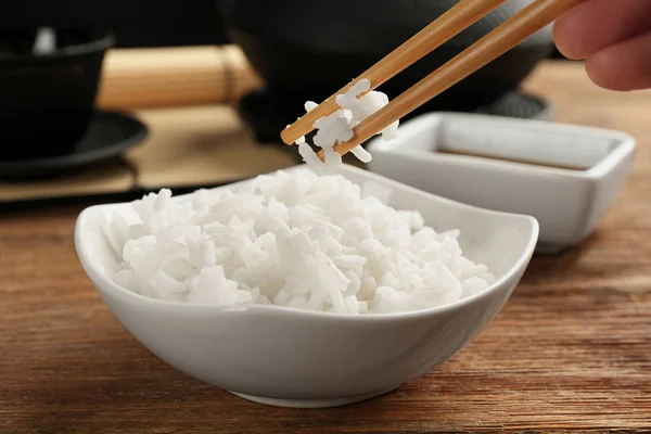 Woman eating rice with chopsticks on wooden table — Stock Photo, Image