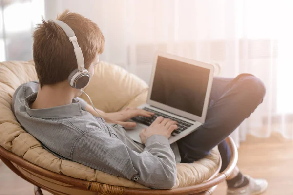 Adolescent travaillant avec un ordinateur portable tout en écoutant de la musique à la maison — Photo