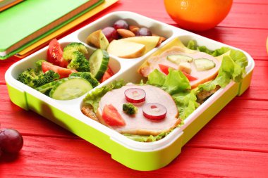 Kırmızı ahşap zemin üzerinde öğle yemeği kutusundaki komik sandviçler