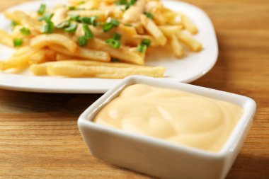 Cheese sauce in small bowl and plate with fries on background clipart