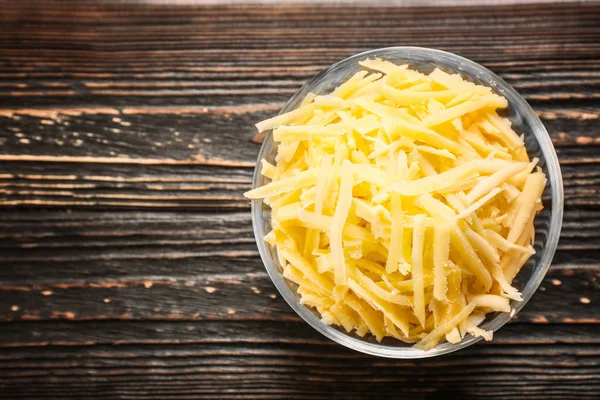 Glass bowl with grated cheese on wooden table — Stock Photo, Image