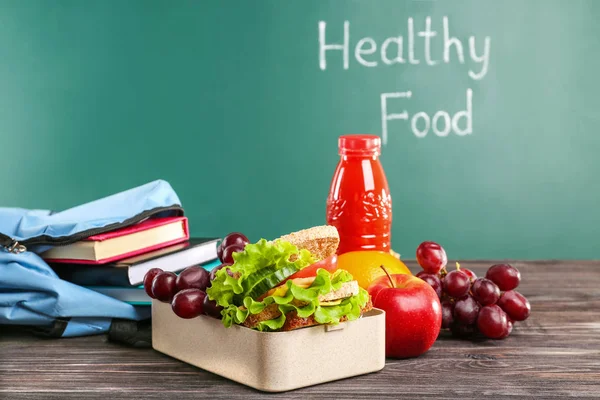 午餐盒与食物、 水果和瓶果汁黑板背景木制的桌子上 — 图库照片
