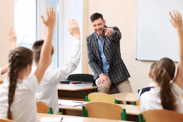 Alumnos escuchando al maestro y levantando las manos para responder en el aula —  Fotos de Stock