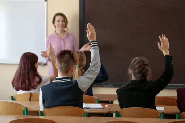 Alumnos escuchando al maestro y levantando las manos para responder en el aula —  Fotos de Stock