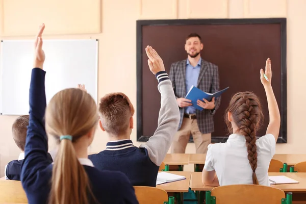 Uczniowie słuchanie nauczyciela i podnoszenie rąk do odpowiedzi w klasie — Zdjęcie stockowe