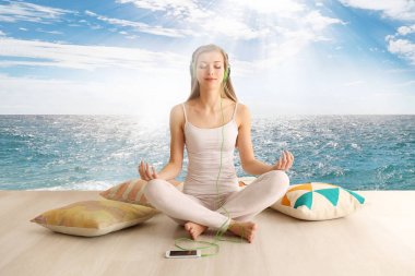 Genç kadın lotus poz deniz manzarası arka plan üzerinde meditasyon. Uyku için müzik kavramı