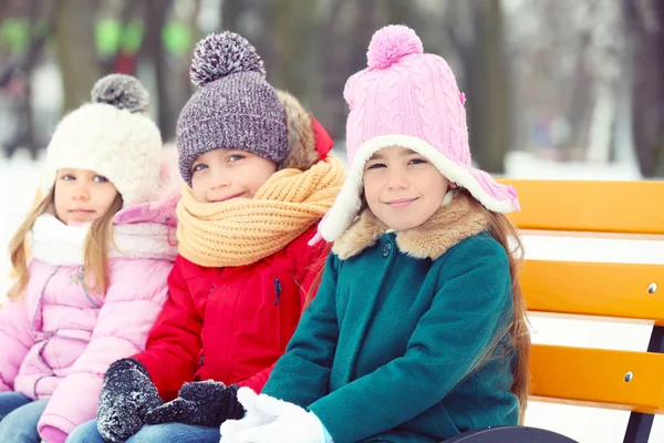Szczęśliwe dzieci siedząc na ławeczce, drewniane, na zewnątrz w zimie — Zdjęcie stockowe