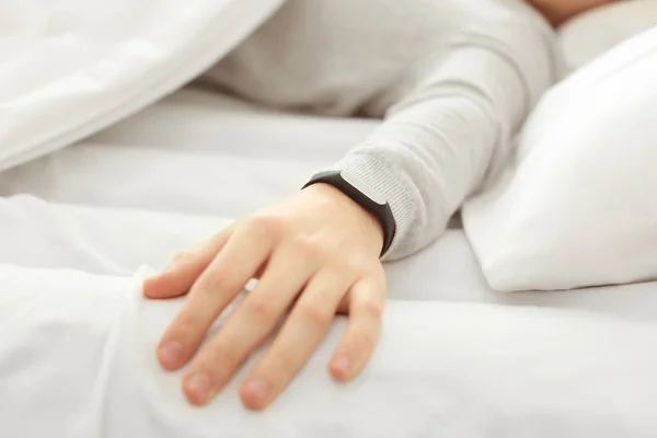Hand of young man with sleep tracker resting in bed at home
