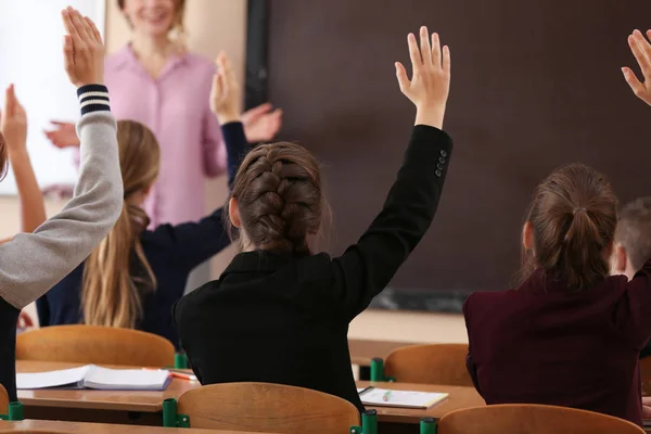 Leerlingen luisteren leraar en verhogen handen te beantwoorden in de klas — Stockfoto