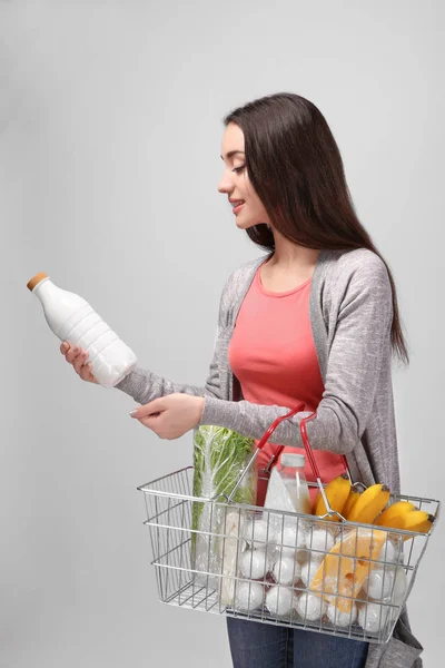 Mujer joven con cesta de la compra completa sobre fondo claro —  Fotos de Stock