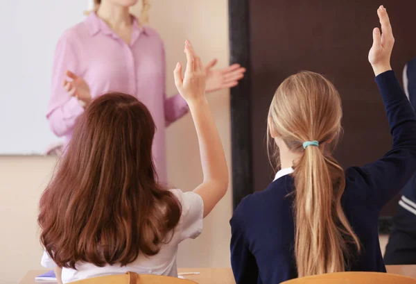 Uczniowie słuchanie nauczyciela i podnoszenie rąk do odpowiedzi w klasie — Zdjęcie stockowe