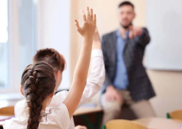 Alunos ouvindo professor e levantando as mãos para responder em sala de aula — Fotografia de Stock