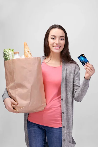 Mujer joven con bolsa de papel de productos sobre fondo claro —  Fotos de Stock
