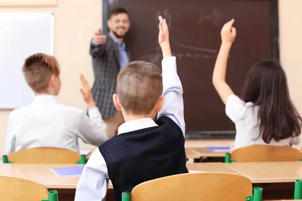 Žáci poslech učitel a zvyšování rukou odpovědět v učebně — Stock fotografie