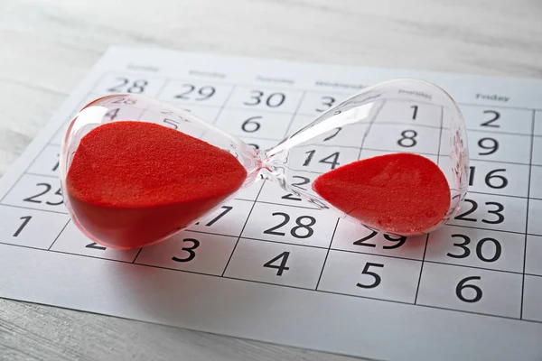 Hourglass with red sand and calendar — Stock Photo, Image