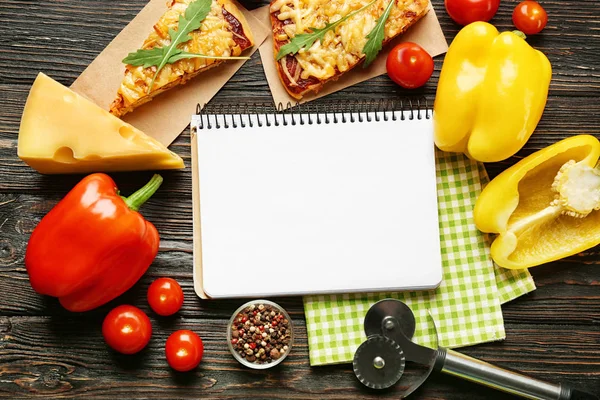 Zátiší s přísadami pro pizzu a recept notebook na dřevěný stůl, pohled shora — Stock fotografie