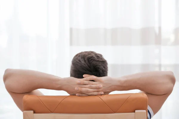 Vista trasera del hombre relajado con las manos detrás de la cabeza sentado en la silla en la habitación de luz — Foto de Stock