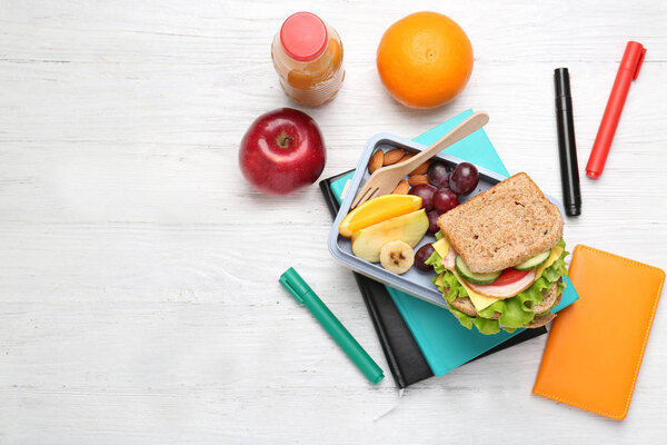 Delicious food in lunch box and stationery on white wooden background