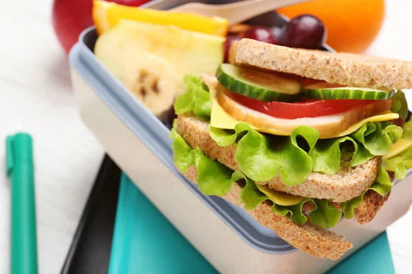 Leckeres Essen in Lunchbox und Schreibwaren auf hellem Hintergrund — Stockfoto