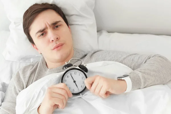 自宅のベッドで横になっている目覚まし時計と若い男 — ストック写真