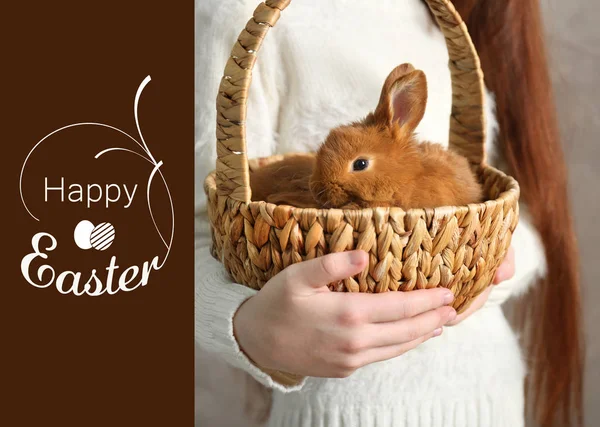 Fille tenant des lapins dans un panier en osier et texte HAPPY EASTER sur fond — Photo