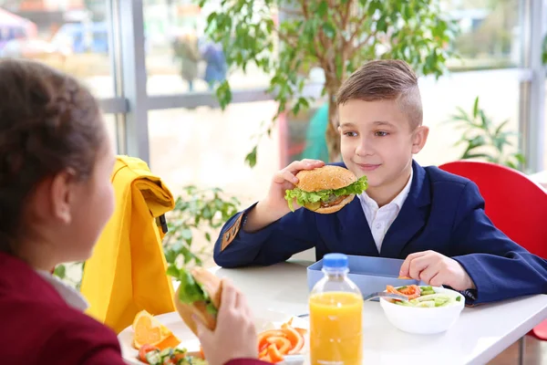 Children sitting at cafeteria table while eating lunch