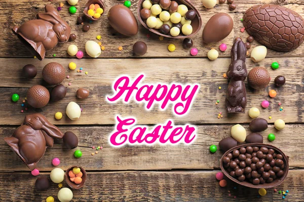 Chocolate treats and text HAPPY EASTER on wooden background — Stock Photo, Image