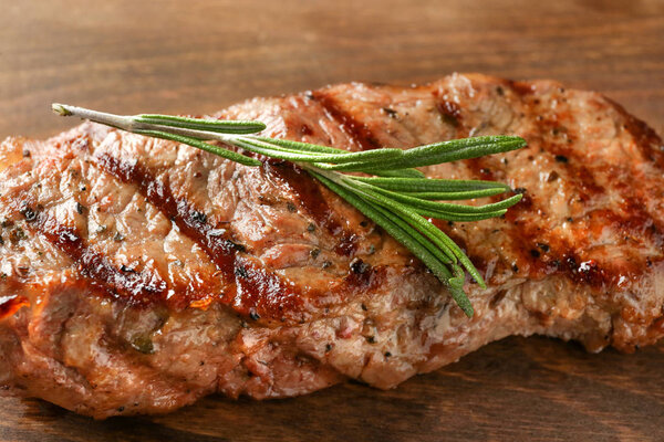 Delicious grilled steak with aromatic rosemary on wooden board, closeup