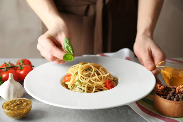 Mujer decorando sabrosa pasta con hojas de albahaca — Foto de Stock