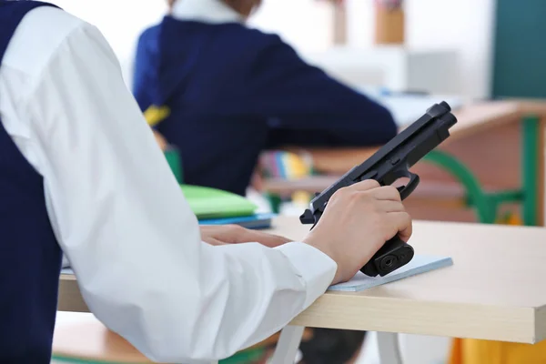 Schoolboy holding gun in classroom — Stock Photo, Image