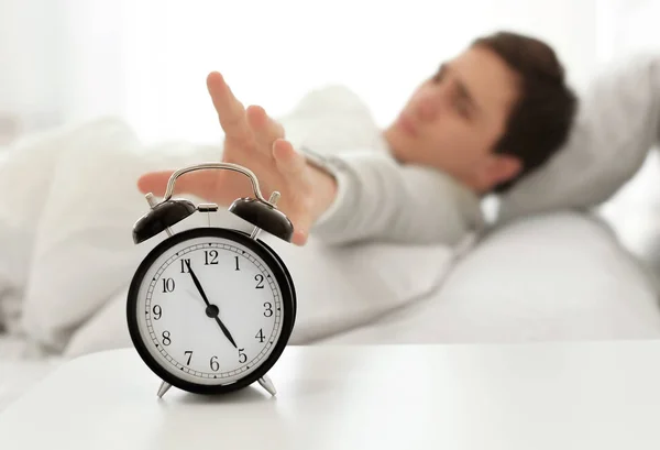 Hombre joven apagando la señal de despertador mientras está acostado en la cama en casa Imagen de stock