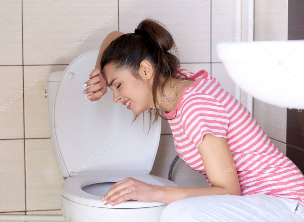 Young vomiting woman near toilet bowl at home