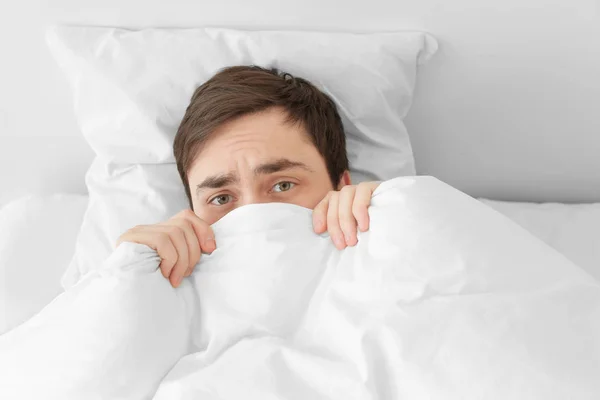 A fiatalember bujkál takaró alatt, miközben ágyban otthon — Stock Fotó