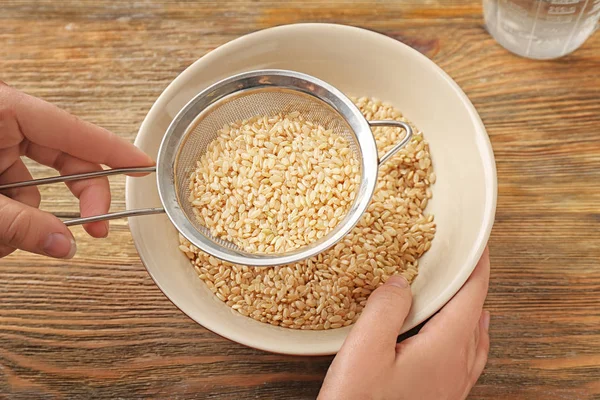 Fêmea mão tigela de enchimento com arroz marrom no fundo de madeira — Fotografia de Stock