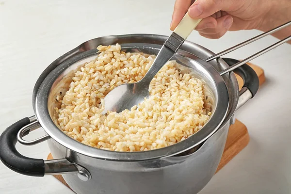 Рука с ложкой перемешивает коричневый рис в дуршлаге — стоковое фото