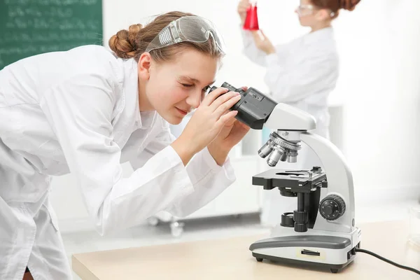 Menina da escola bonita olhando através do microscópio na aula de química — Fotografia de Stock