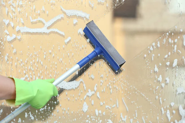 Hand with mop washing window