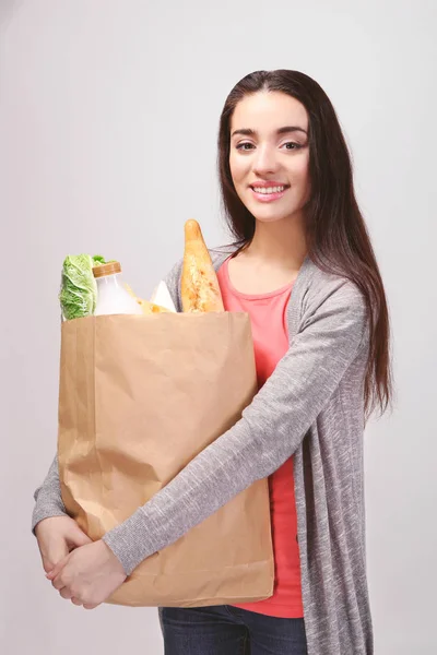 Mujer joven con bolsa de papel de productos sobre fondo claro —  Fotos de Stock