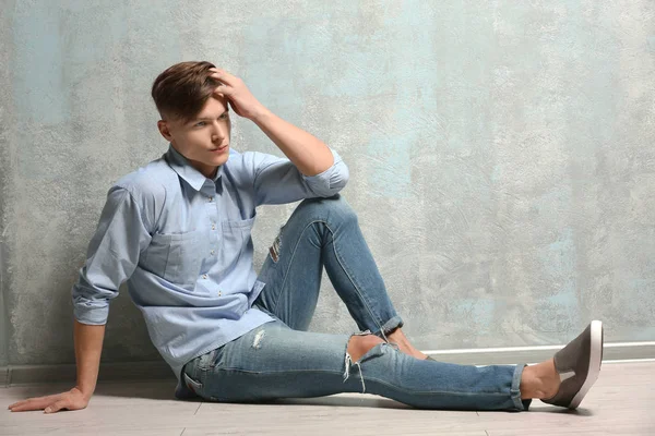 Handsome young man sitting on floor near textured wall — Stock Photo, Image