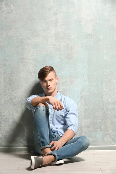Handsome young man sitting on floor near textured wall — Stock Photo, Image