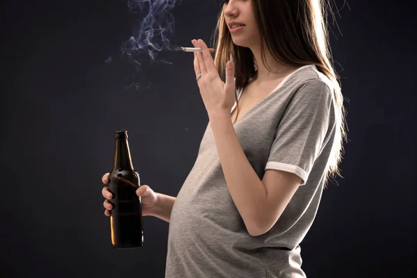 Pregnant woman smoking cigarette and drinking beer on dark background — Stock Photo, Image